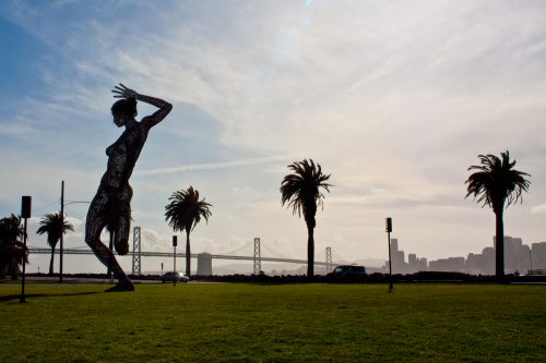 burning man statue on treasure island, with bay bridge and san francisco skyline in the background, california